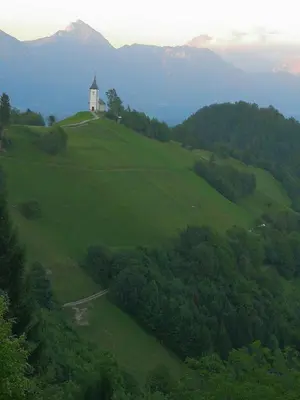 a church on top of a green hill with trees at Apartments Na Žagi in Železniki