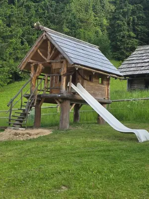 a wooden playground with a slide and a house at Brunarica Bled Zatrnik Pokljuka in Bled