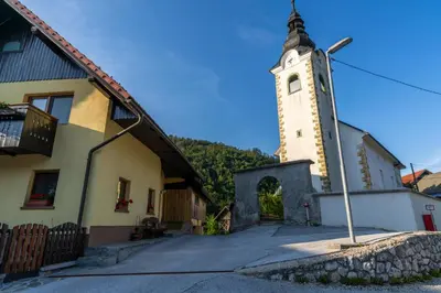 a church with a clock tower next to a building at Sobe na skednju in Bohinjska Bistrica