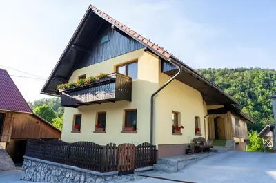 a yellow house with a black roof and a balcony at Sobe na skednju in Bohinjska Bistrica