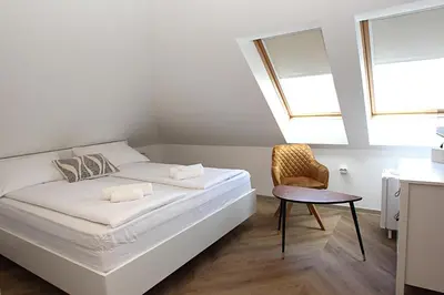 a white bedroom with a bed and a chair at D Rooms in Ljubljana