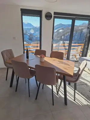 a wooden table and chairs in a room with windows at En hribček in Ptujska Gora
