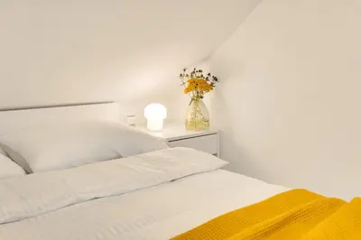 a white bedroom with a bed and a vase of flowers at Lux House Natura with Sauna & Hot Tub