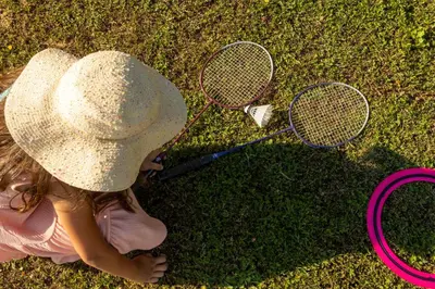 a little girl sitting on the grass with two tennis rackets at Lux House Natura with Sauna & Hot Tub