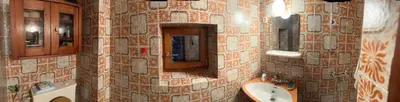 a bathroom with a tiled wall with a sink and mirrors at Hiša p'r Kobalu in Idrija