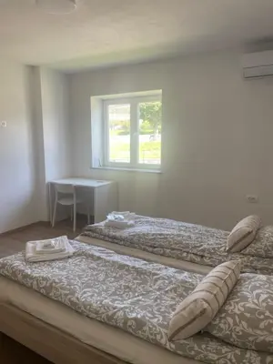 two beds in a room with a table and a window at VP sobe in Ilirska Bistrica