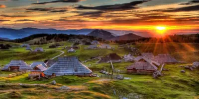 a painting of a group of huts on a hill at sunset at Hiša pod Veliko planino in Stahovica