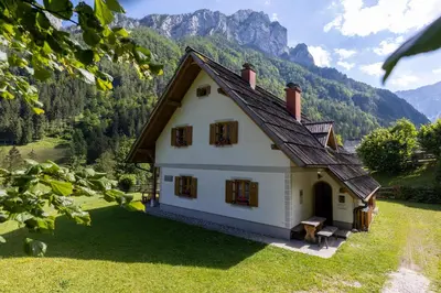 a small white house with mountains in the background at Mala hiša in Solčava
