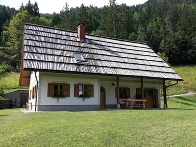 a white house with a metal roof on a field at Mala hiša in Solčava
