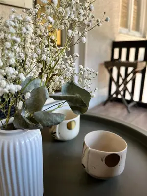 a table with a vase and a cup and flowers at Cukr in Ljubljana