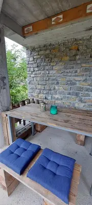 a wooden picnic table with blue cushions in front of a brick wall at Počitniška hiška v grapi in Tolmin
