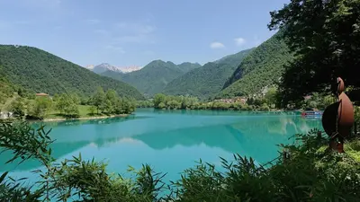a person sitting on the edge of a lake with mountains at Hiša Nad Reko Baca in Most na Soči