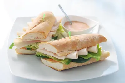 two sandwiches on a plate with a bowl of dipping sauce at Cacao Rooms in Ljubljana
