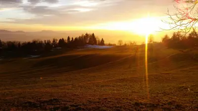 a sunset on a field with the sun setting on the horizon at Turizem Pavlin Apartments in Šenturska Gora