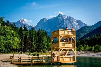 a wooden tower in the water with mountains in the background at Apartments Demec in Kranjska Gora
