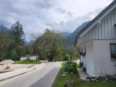 a road next to a white building with a mountain at Bovec Comfortable Apartment with Mountain View - One Bedroom Apartment with Mountain View in Bovec
