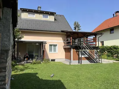 a house with a balcony and a man sitting in a yard at Meadow Tranquil Apartments with Evergreen Garden - Studio Apartment in Žirovnica