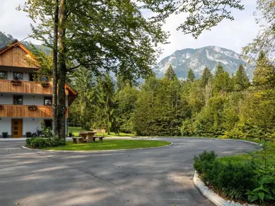 a winding road in front of a building with mountains in the background at The Woodland Nook Apartments Bohinj - Classic Two Bedroom Apartment with Balcony in Bohinj
