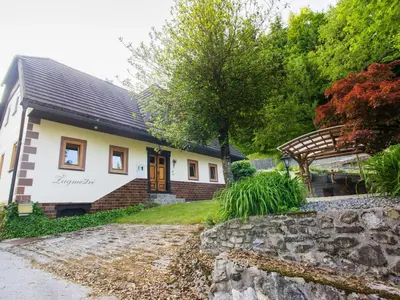 a small white house with a porch and a stone wall at Rustic Authentic Holiday Home with Terrace and Wood Stove - Three Bedroom Holiday Home with Terrace in Ljubno