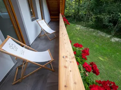 two chairs sitting on a porch with red flowers at The Woodland Nook Apartments Bohinj - Comfort Two Bedroom Apartment with Balcony in Bohinj