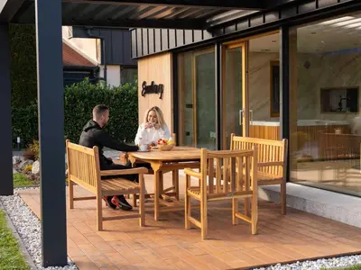 a man and woman sitting at a wooden table on a patio at Elegant Warm Bliss Hideaway Escape Lodge - Holiday Home with Hot-Tub and Sauna in Šenčur