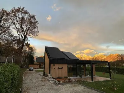 a small house with a black roof with mountains in the background at Elegant Warm Bliss Hideaway Escape Lodge - Holiday Home with Hot-Tub in Šenčur