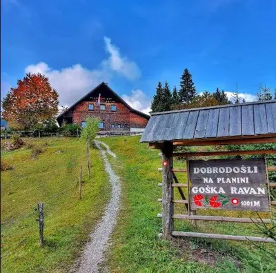 a sign in front of a building in a field at planinski dom Goška Ravan in Kamna Gorica