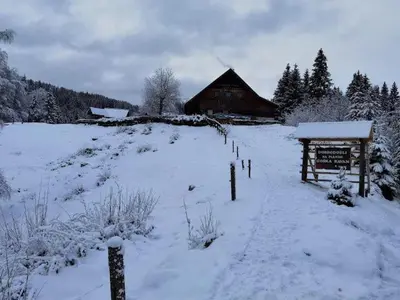 a snow covered field with a barn and a sign at planinski dom Goška Ravan in Kamna Gorica