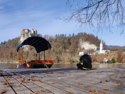 a man sitting on a dock next to a boat at Cozy rooms in the center of Bled by the lake #1 in Bled