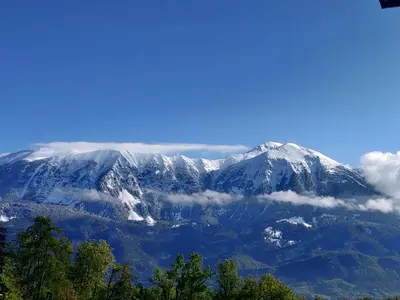 a snow covered mountain with clouds in front of it at Cozy rooms in the center of Bled by the lake #1 in Bled