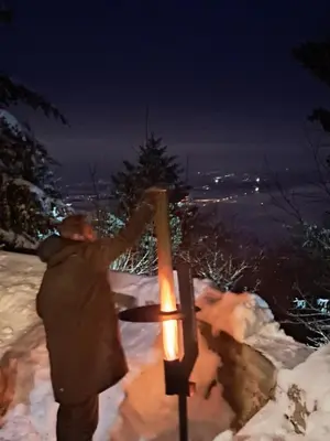 a man holding a candle in the snow at night at Gostišče Jelka in Pohorje