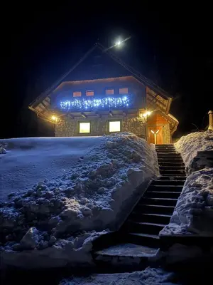 a house with lights on it in the snow at Private Forest Cabin with Epic View in Ribnica na Pohorju