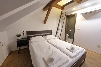 a bedroom with a bed with white sheets and a ladder at AMS Rooms in Ljubljana