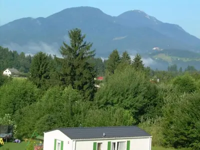 a house in a field with mountains in the background at Apartment Stacaravan Rozika Slowenien by Interhome in Slovenj Gradec