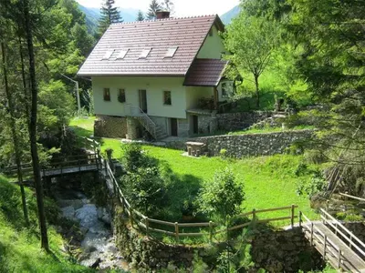 a house on a hill with a stream in front of it at Holiday Home Geräumiges Ferienhaus inmitten der Natur by Interhome in Dolenja Trebuša