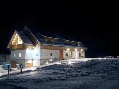 a house in the snow at night with lights at Gostišče Jezersko in Zgornje Jezersko