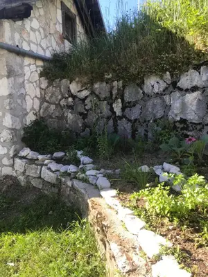 a stone wall next to a garden with flowers at Penzion Sinji vrh in Zoll