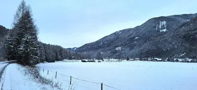 a snow covered field with a fence in front of a mountain at River2Mountain Cozy Apartment in Gozd Martuljek