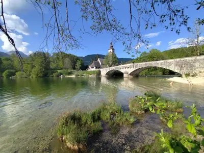 a bridge over a river with a church in the background at Apartma jezero MIG in Bohinj