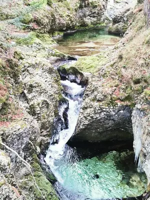 a waterfall on a rocky hill with green water at Apartma jezero MIG in Bohinj