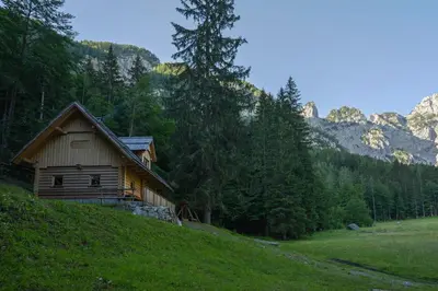 a wooden cabin on a hill with mountains in the background at Alpine Loghouse Planšarska bajta Matkov Kot in Solčava