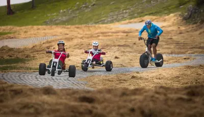 three people riding on tricycles on a dirt road at Apartmajska hiša Muštrinka in Cerklje na Gorenjskem