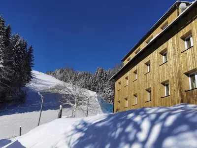 a building in the snow next to a mountain at APARTMENTS ROGLA JURGOVO - Ski in Ski out in Lukanja