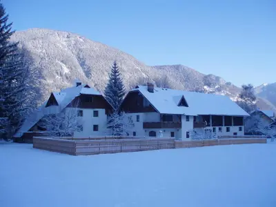 a building with snow on it in front of a mountain at Turistična kmetija Košir in Kranjska Gora