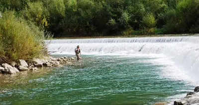 a man is standing in a river in front of a waterfall at Farm Stay Žagar in Mozirje