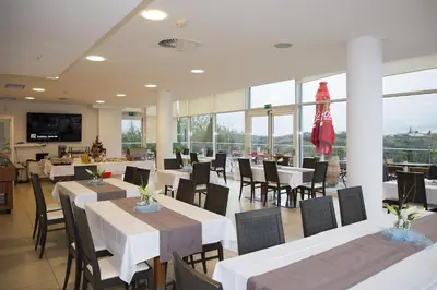 a restaurant with white tables and chairs and windows at Hotel Kozana in Dobrovo