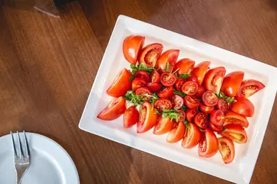 a white plate with carrots and tomatoes on a table at Casino & Hotel ADMIRAL Kozina in Kozina