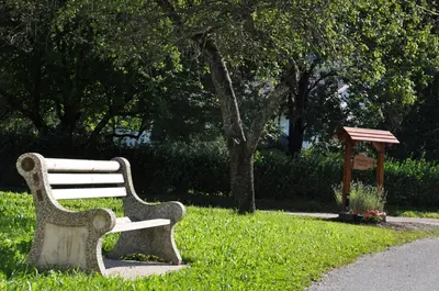 a park bench sitting in the grass near a tree at Apartment Mlinarjeva domačija in Kobarid