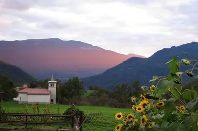 a church in a field with mountains in the background at Tourist Farm Žvanč in Kobarid