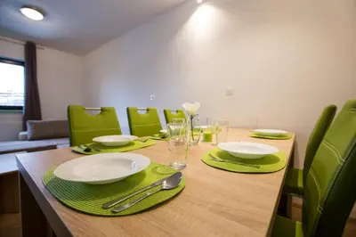 a dining room table with green chairs and a wooden table with plates and glasses at Podkoren Apartments in Kranjska Gora